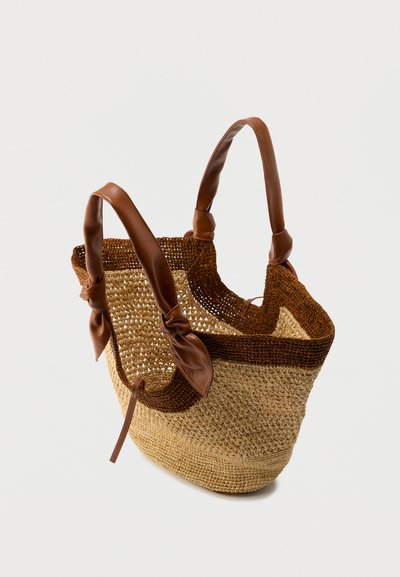 Πλεκτή τσάντα χόρτου με καφέ λουράκια από δέρμα. Διαθέτει υφασμάτινο σχέδιο, ανοιχτό επάνω μέρος και δεμένα ντεκόρ για λεπτομέρειες.