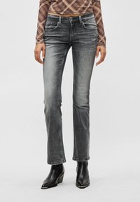 Γκρι τζιν με ίσια γραμμή, ξεθωριασμένο φ ινίρισμα, πέντε τσέπες και μεταλλικά εξαρτήματα. Συνδυασμένο με πουκάμισο μακρυμάνικο με σχέδιο και μποτάκια μέχρι τον αστράγαλο.