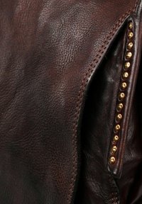 Donkerbruin leren stof met een gestructureerde nerf, gedetailleerde stiksels en een rij kleine, ronde, goudkleurige studs langs de rand.