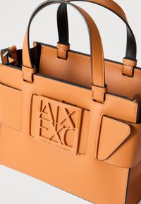 Καφέ δερμάτινη τσάντα με δύο λαβές, με ανάγλυφη πλακέτα λογότυπου Armani Exchange στο μπροστινό μέρος και ραφές διακοσμητικές.