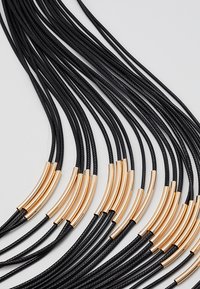 Collar de múltiples hilos que presenta cuerdas trenzadas en negro con acentos curvados en dorado, creando una textura elegante y en capas.