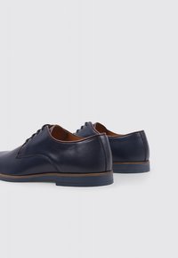Chaussures en cuir bleu marine foncé avec un bout rond, texture lisse, doublure intérieure marron et semelle contrastante en marron clair. Conception à lacets avec un minimum de surpiqûres.
