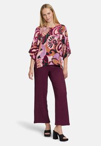 Haut fluide à motifs avec des fleurs roses, bordeaux et lavande ; associé à un pantalon large bordeaux texturé et des sandales à plateformes noires.