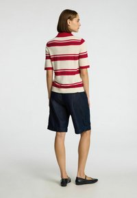 Korte mouwen gestreepte polo in crème met rode en bordeauxstrepen, gecombineerd met donkerblauwe denim shorts. Heeft een ontspannen pasvorm en platte schoenen.