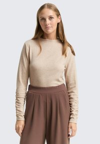 Beige top met lange mouwen gemaakt van zachte stof, met een ronde halslijn en licht geplooide mouwen, gecombineerd met high-waisted bruine broek.