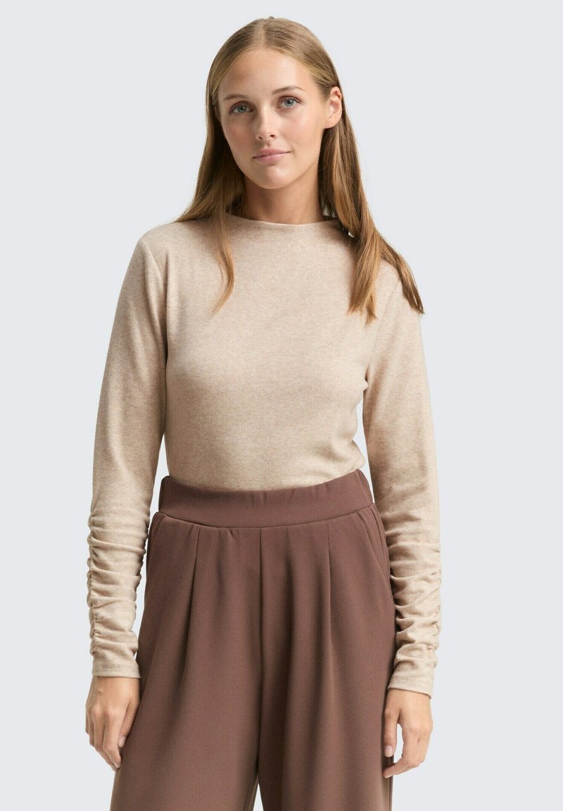 Beige top met lange mouwen gemaakt van zachte stof, met een ronde halslijn en licht geplooide mouwen, gecombineerd met high-waisted bruine broek.