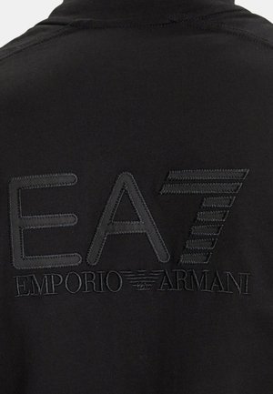 Tela negra con el logo EA7 bordado y la marca Emporio Armani en hilo negro en la parte trasera de una prenda.