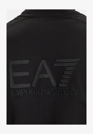 Tela negra con el logo EA7 bordado y la marca Emporio Armani en hilo negro en la parte trasera de una prenda.
