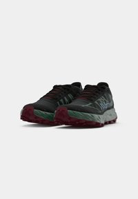 Ein Paar schwarze und grüne Trailrunning-Schuhe mit roten Schnürsenkeln und Sohlen, die ein robustes Profil und das Markenlogo an der Seite zeigen.