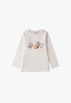 T-shirt a maniche lunghe color crema con un volto di orso stampato, un fiocco blu e il testo "JOY" in grigio e nero. Tessuto di cotone morbido, scollatura rotonda.