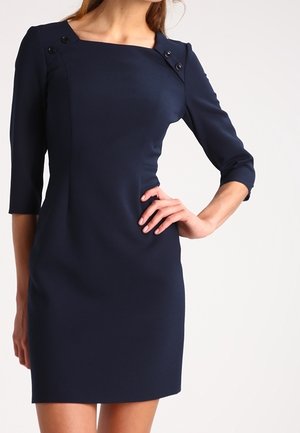 Robe ajustée bleu marine à manches trois-quarts, décolleté carré et boutons décoratifs aux épaules. Texture lisse, design longueur genou.
