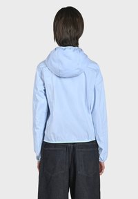 Giacca con cappuccio di colore azzurro chiaro, con polsini ed orlo elasticizzati, realizzata in materiale liscio. La vista posteriore mostra le cuciture e una vestibilità rilassata.