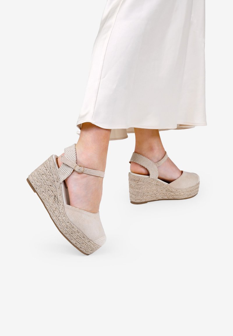 Sandalias de cuña beige con un upper de tela texturizada, plataforma de yute trenzado y correa para el tobillo con cierre de hebilla.