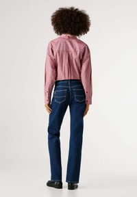 Ριγέ κοντομάνικο πουκάμισο με κόκκινες και λευκές ρίγες και μανσέτες με κουμπιά, συνδυασμένο με σκουρόχρωμα μπλε τζιν παντελόνια με πίσω τσέπες, φορεμένο με μαύρα παπούτσια.