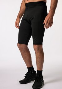 Shorts de sport noirs en matière extensible, présentant un design ajusté, une texture lisse et une large ceinture avec un logo.