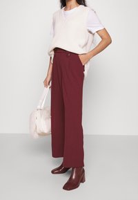 Ljus krämfärgad stickad väst över en vit t-shirt, tillsammans med mörk borgå wide-leg byxor. Bruna klackbottnar och en mjuk rosa handväska.