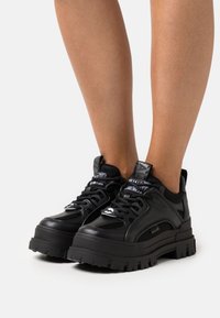 Black sneakers with a chunky sole, made of leather and mesh. Features padded tongue, textured accents, and contrasting laces for secure fit.