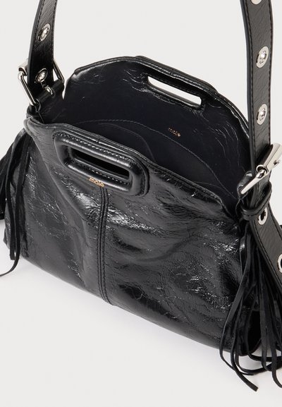 Sac à main en cuir noir brillant avec poignées découpées rectangulaires, bandoulière réglable avec œillets métalliques et détails de franges à pompons.