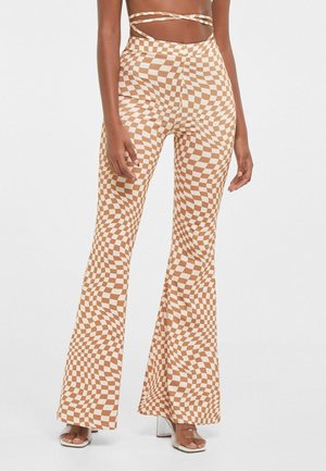 Checkered flared pants in brown and white, featuring a fabric with a distorted pattern. Design includes high waist and flowy legs.