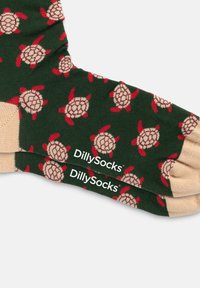 Grüne Socken mit einem Schildkrötenmuster, versehen mit roten und beigen Akzenten. Das Material wirkt weich; die Marke "DillySocks" ist in der Nähe der Zehenpartie sichtbar.