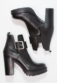 Botas de tobillo negras con tacón y suela gruesa, con detalle de hebilla lateral, posicionadas en un ángulo sobre un fondo blanco.