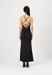 Črna maksi obleka z oprijetim korzetom, križnimi naramnicami na hrbtu in zavezanim pasom. Narejena iz gladkega materiala z elegantno silhueto.