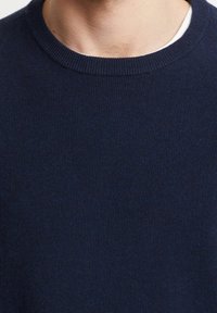 Mörkblått stickat tröja med ribbad rundhals, som har en fin struktur och en tight passform.