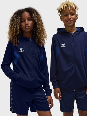 Twee jonge mensen dragen marineblauwe Hummel hoodies met rits en shorts, staand naast elkaar tegen een effen achtergrond.