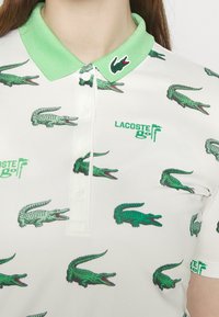 White polo shirt featuring green crocodile patterns, a light green ribbed collar, and a green embroidered logo on the chest.