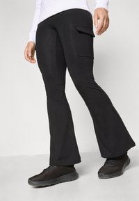 Svarta utsvängda byxor med en sidoficka i cargo-stil. Gjorda av ett stretchy material, har de en slät yta och en figursydd midja. Kombineras med svarta sneakers.