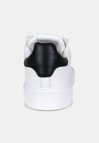 Sneaker bianco con tallone in pelle nera, forma arrotondata, lati texturizzati e suola in gomma bianca. Design minimalista senza motivi visibili.