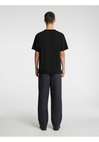 Melnas kokvilnas T-krekls ar īsām piedurknēm, apaļu kakla izgriezumu, kombinēts ar vaļīgām tumši ziliem biksēm. Vienkāršs dizains, bez redzamām logotipām vai rakstiem.