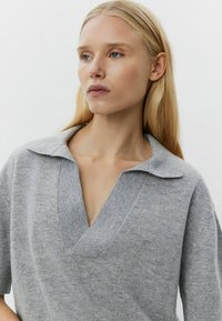 Szürke kötött pulóver széles gallérral és Vnyakú kivágással. Puha textúra, laza fazon és rövid ujjú. Finom melankó hatás az anyagon.