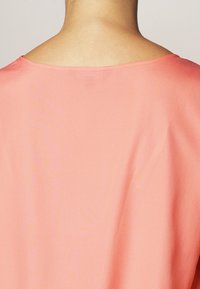Kortærmet, koralfarvet bluse. Glat stof med en afslappet pasform og en bred halsudskæring. Enkel, ren design uden synlige mønstre eller detaljer.