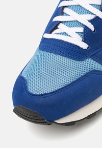 Modrá sportovní obuv s svrchním materiálem z semiše a síťoviny, texturovanou modrou síťovinou, bílými tkaničkami a černou gumovou podešví.