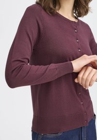 Burgunderfarbener Cardigan in einer figurschmeichelnden Passform mit Rundhalsausschnitt. Verfügt über lange Ärmel, gerippte Bündchen und Knopfdetails auf der Vorderseite.