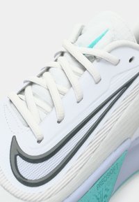Baskets blanches avec tige en mesh, détail en swoosh noir et accents turquoise. Présente des lacets plats et une semelle intercalaire texturée.