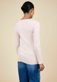 Pikkade varrukatega sooniktop pehmes roosas, ümmarguse kaeluse ja veidi vormitud siluetiga, koos siniste teksapüüksidega.