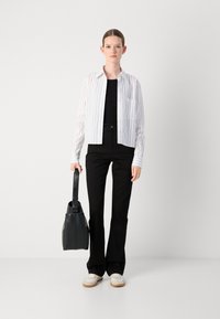 Chemise à rayures blanche et bleu clair, jeans noirs, sac fourre-tout noir et baskets blanches avec semelles beige.