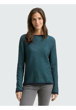 Pull en teal texturé à manches longues, col rond, avec des accents côtelés aux poignets et à l'ourlet, associé à un jean gris.