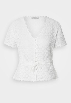 Hvit, kortermet bluse med V-hals, teksturert blomstermønster, knappetransfront og knyttet livbelte. Har scalloperte kanter.