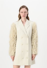 Robe blazer croisée en ivoire avec des manches transparentes et volantes. Présente une coupe ajustée, cinq boutons et une texture lisse.