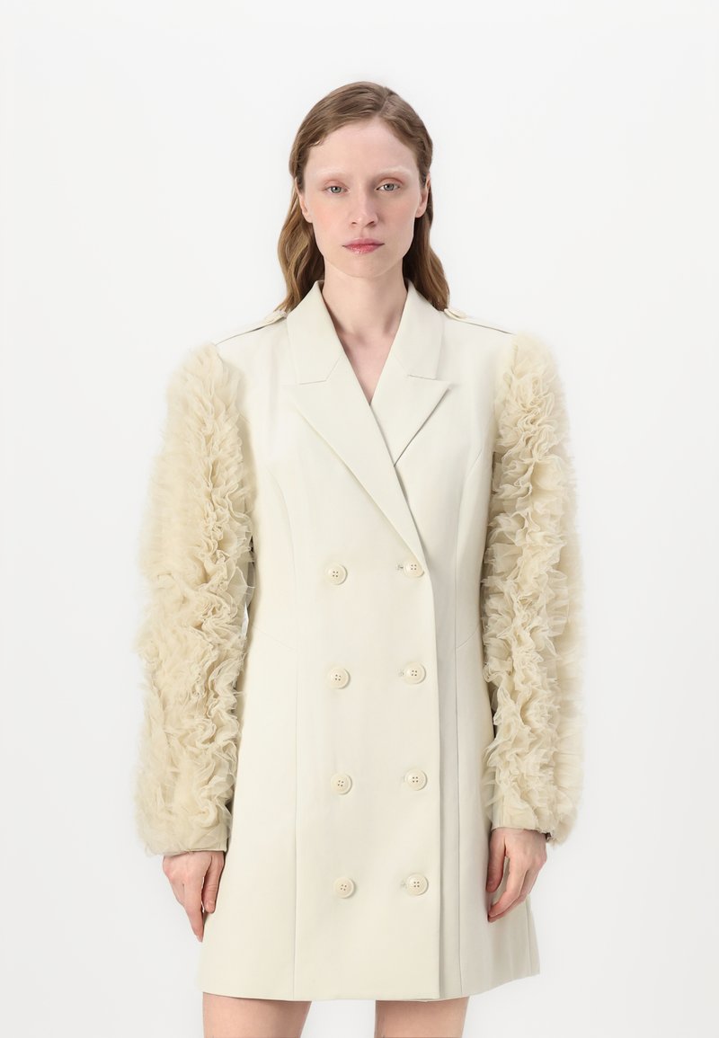 Robe blazer croisée en ivoire avec des manches transparentes et volantes. Présente une coupe ajustée, cinq boutons et une texture lisse.