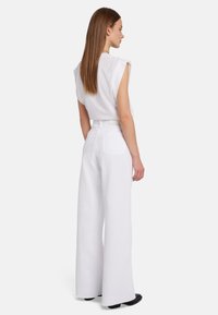 Top corto bianco e pantaloni a gamba larga. Realizzati in un tessuto leggero con una texture liscia. Include passanti per cintura e due tasche posteriori.