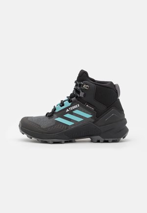 Zwart en grijs wandelboot met turquoise strepen, hoge enkelondersteuning, robuuste zool en vetersluiting, ontworpen voor gebruik buitenshuis.