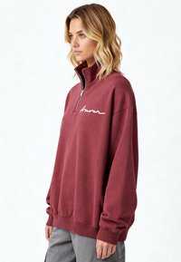 Sweat-shirt bordeaux à zip avec col montant, orné d'un texte brodé blanc "Amour", coupe décontractée, poignets et ourlet côtelés.