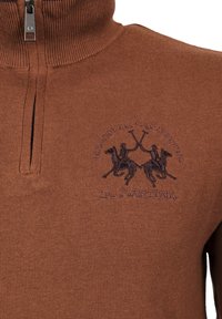 Pull en maille marron avec col zippé, présentant une scène de polo brodée et le nom de la marque en violet foncé. Finition en tissu texturé.