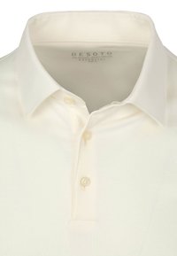 Crème polo-shirt met een klassieke kraag, drie knoopsluitingen en een gladde textuur zonder patronen. Etiket leest "DESOTO."