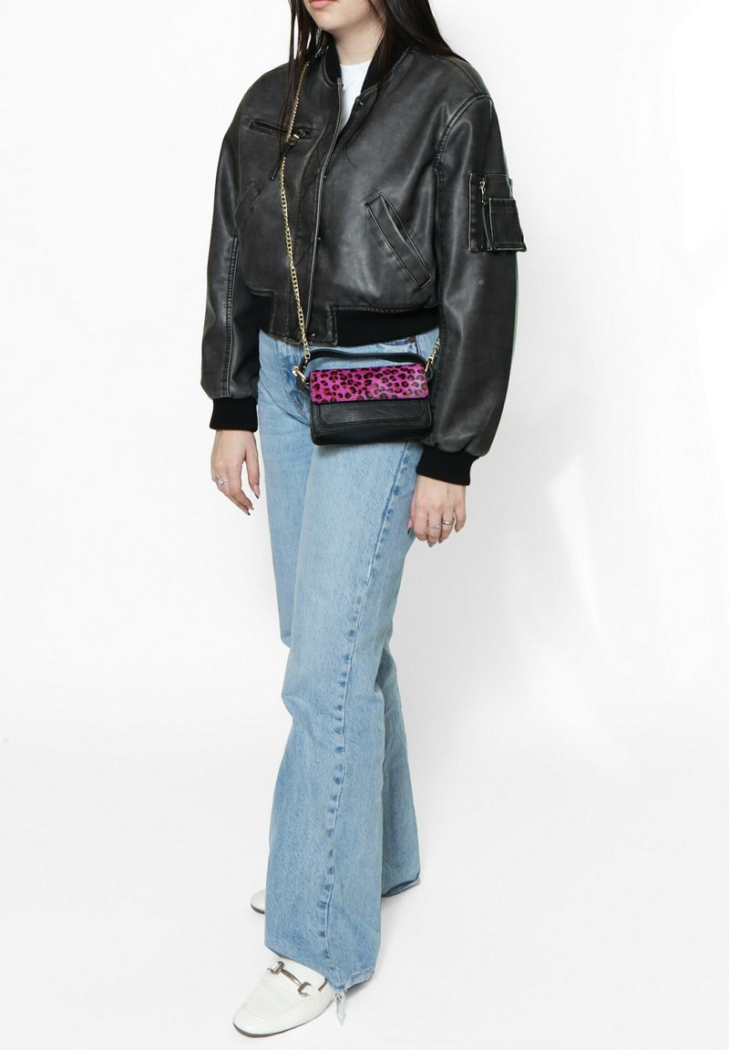 Giubbotto bomber in pelle nera con polsini a costine, jeans flare azzurri chiari e una piccola borsa a tracolla con un design a stampa leopardata rosa.