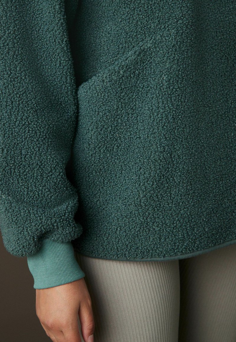 Fleece pullover i mørk havblå, med en tekstureret overflade, elastiske manchetter og en afslappet pasform. Stylet med ribbede beige leggings.